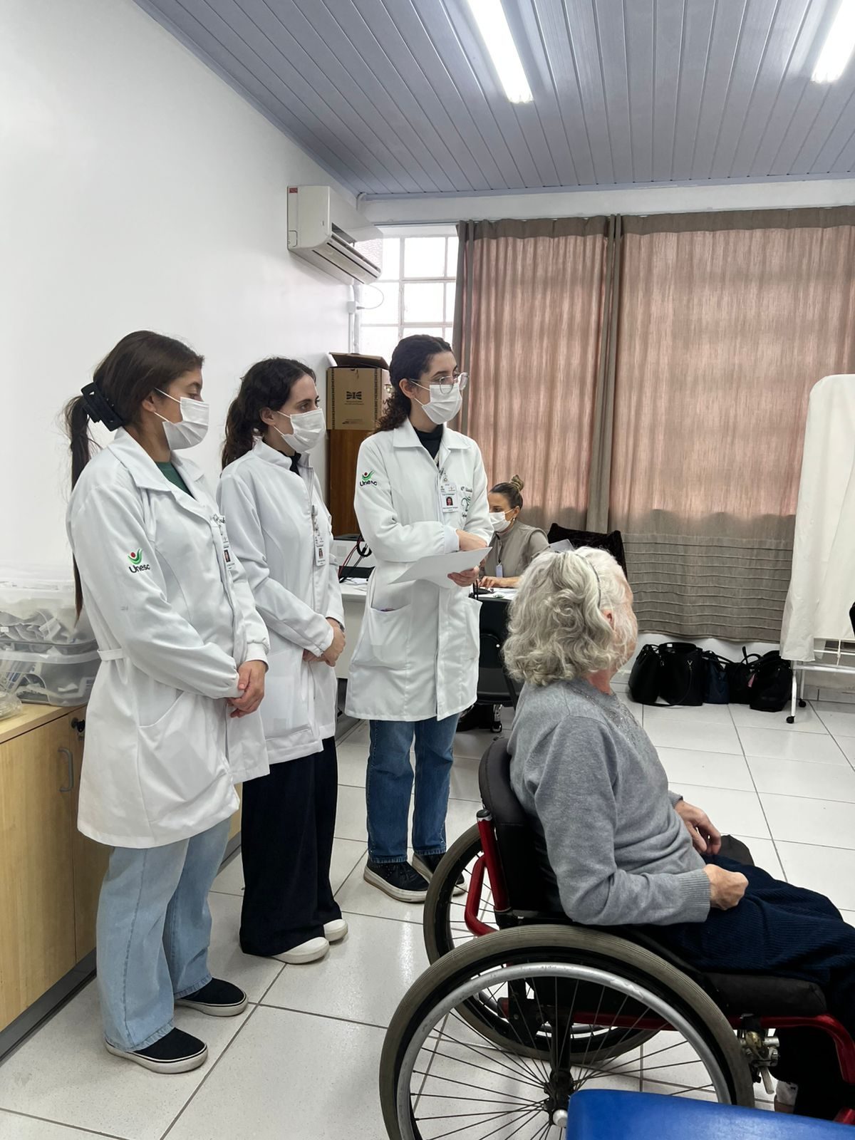 Equipe multiprofissional da Associação Vida Ativa São José, de jaleco, ao lado de um usuário em cadeira de rodas